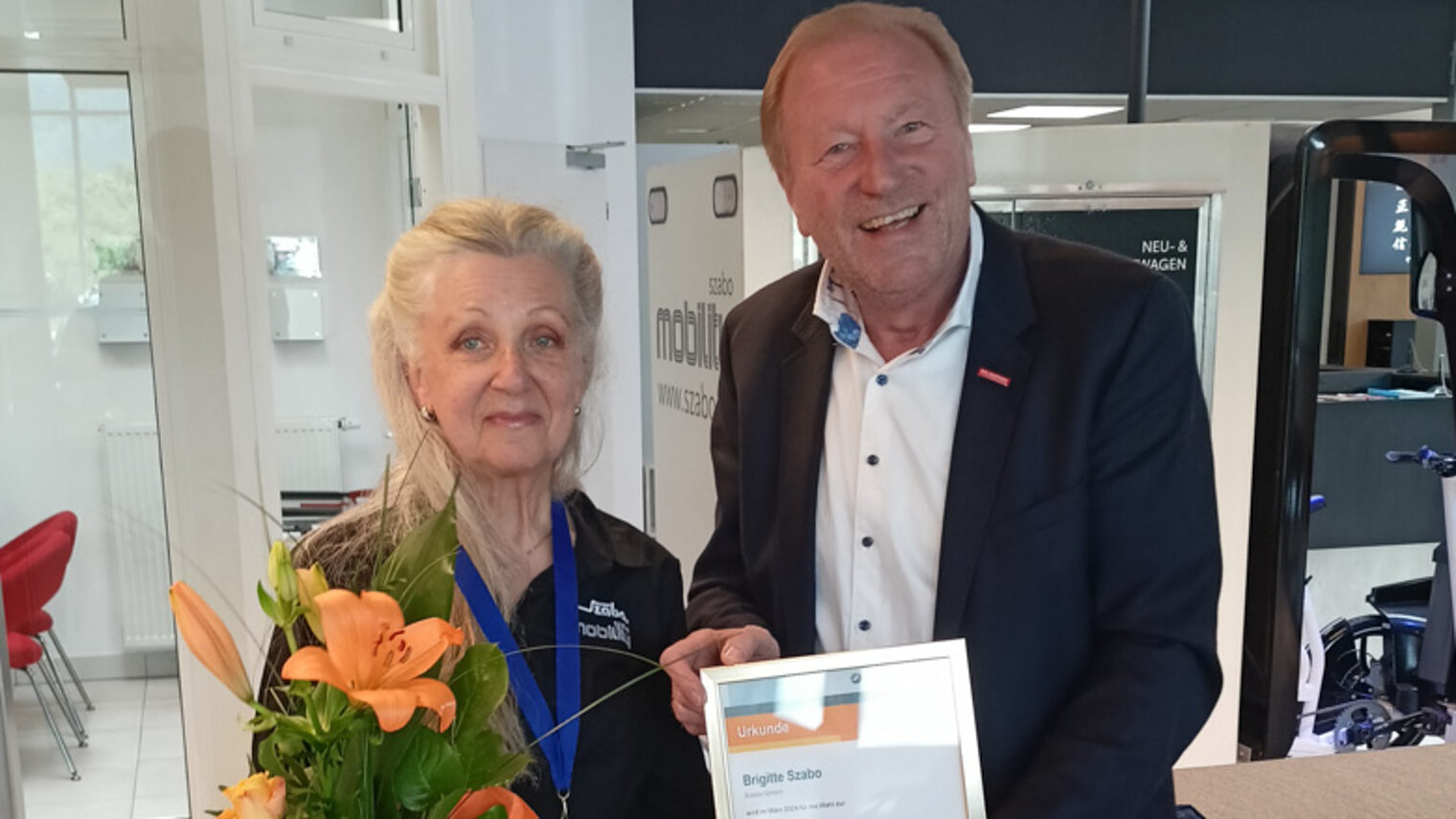 Ulrich Bopp überreicht Brigitte Szabo eine Auszeichnung mit Urkunde und einem Blumenstrauß