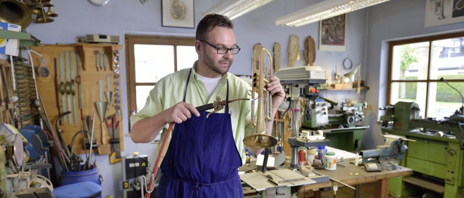 Handwerker steht in seiner Werkstatt und bearbeitet eine Trompete. 
