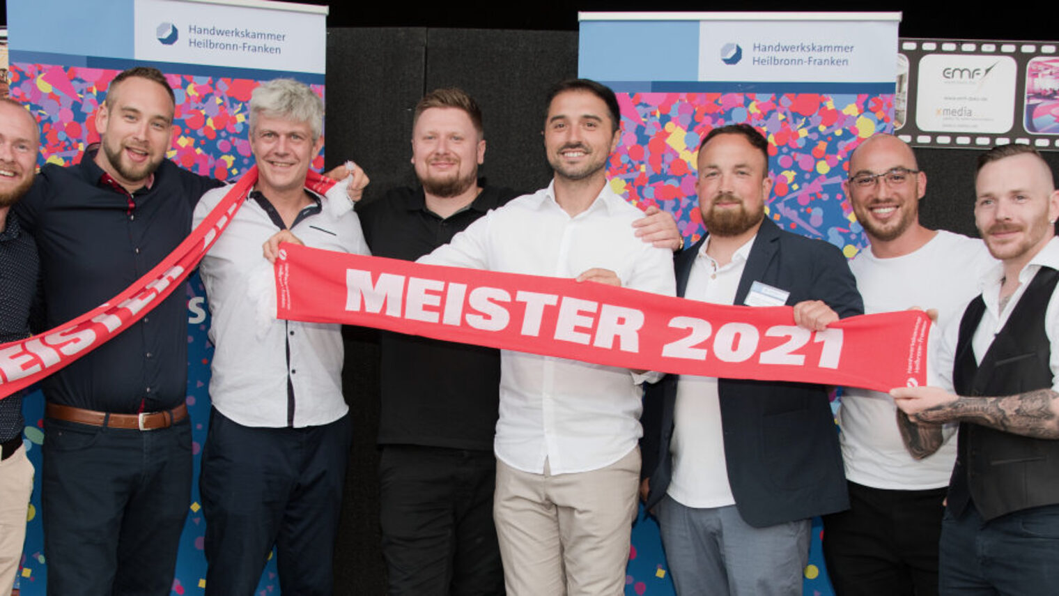 Eine Gruppe von Männern steht nebeneinander und hält zwei rote Schals mit weißer Aufschrift "Meister 2021" in den Händen.