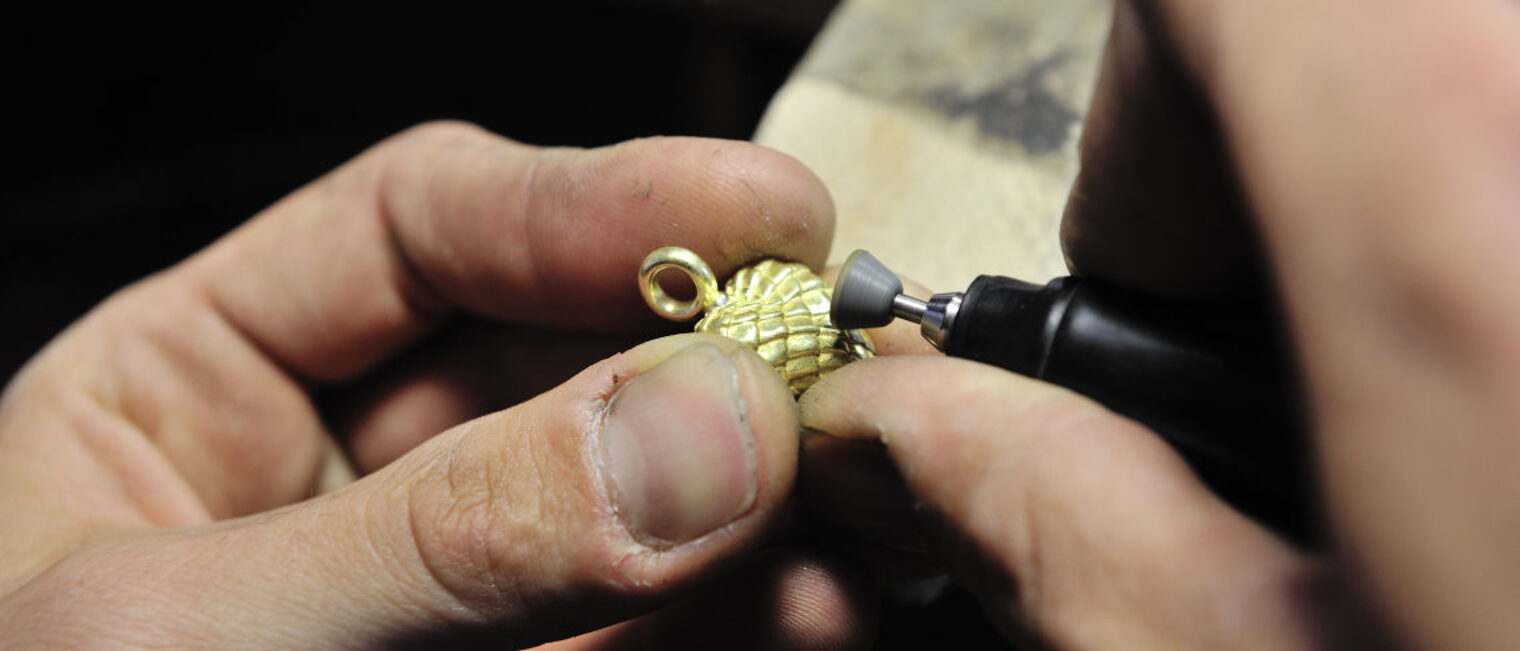 Die Hände eines Goldschmieds bei der Bearbeitung eines Schmuckstücks.