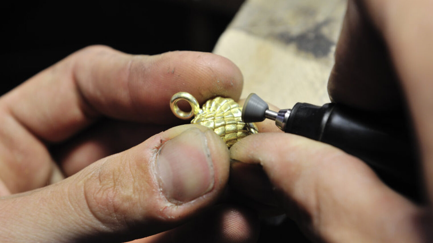 Die Hände eines Goldschmieds bei der Bearbeitung eines Schmuckstücks.