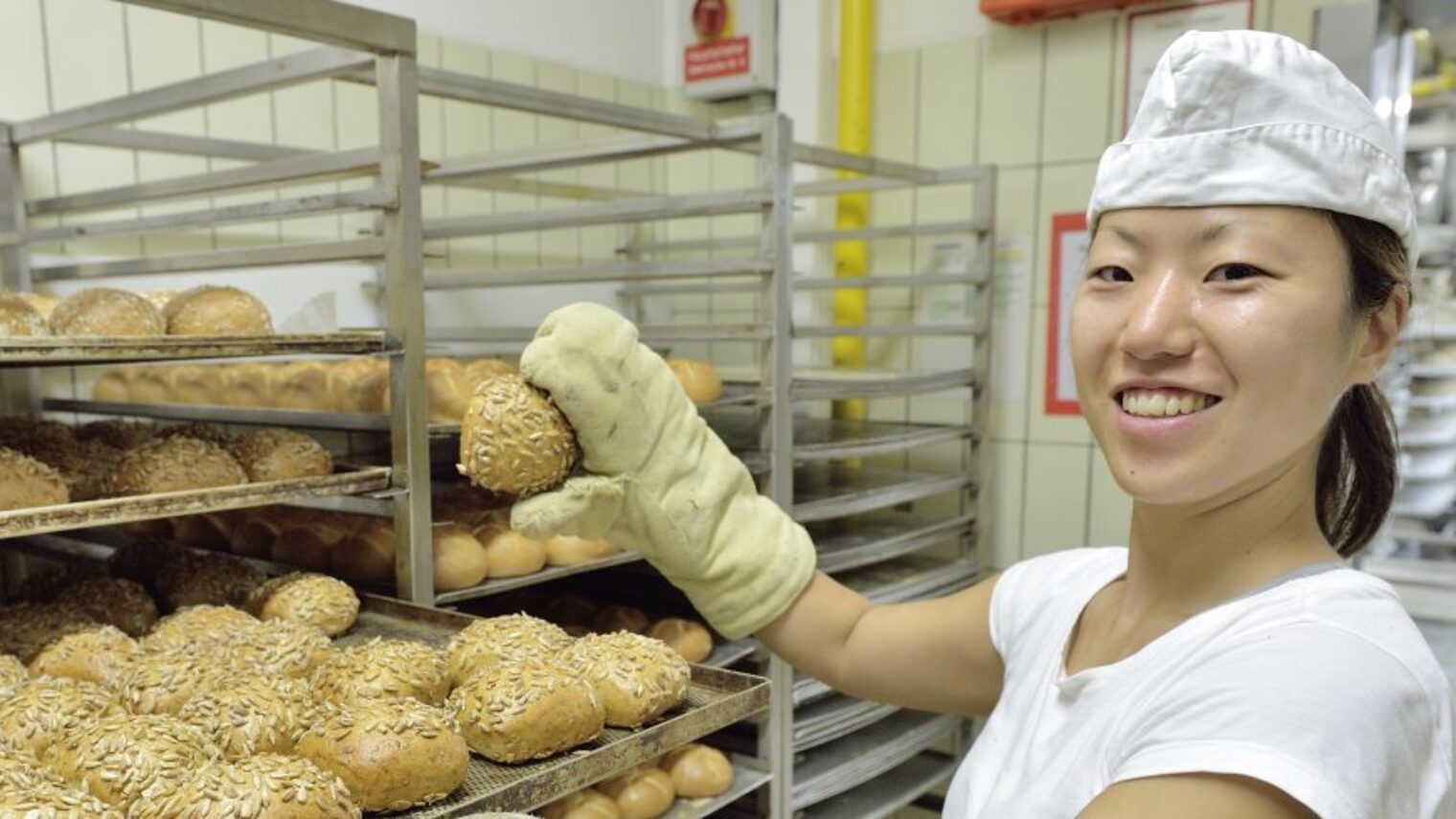 Eine Bäckerin mit asiatischer Herkunft arbeitet in einer Backstube.