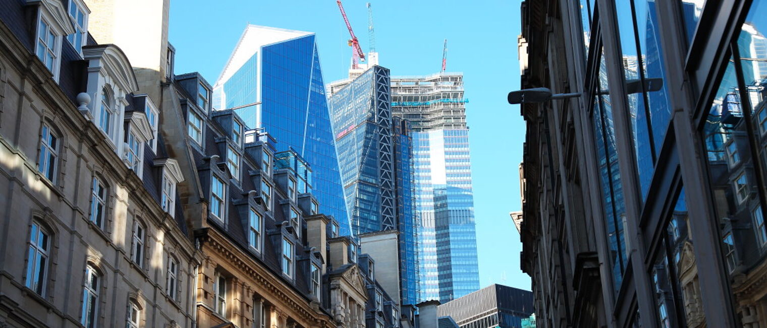 In den Straßen von London sieht man historische und moderne Gebäude, im Hintergrund gibt es Wolkenkratzer mit Baukränen.