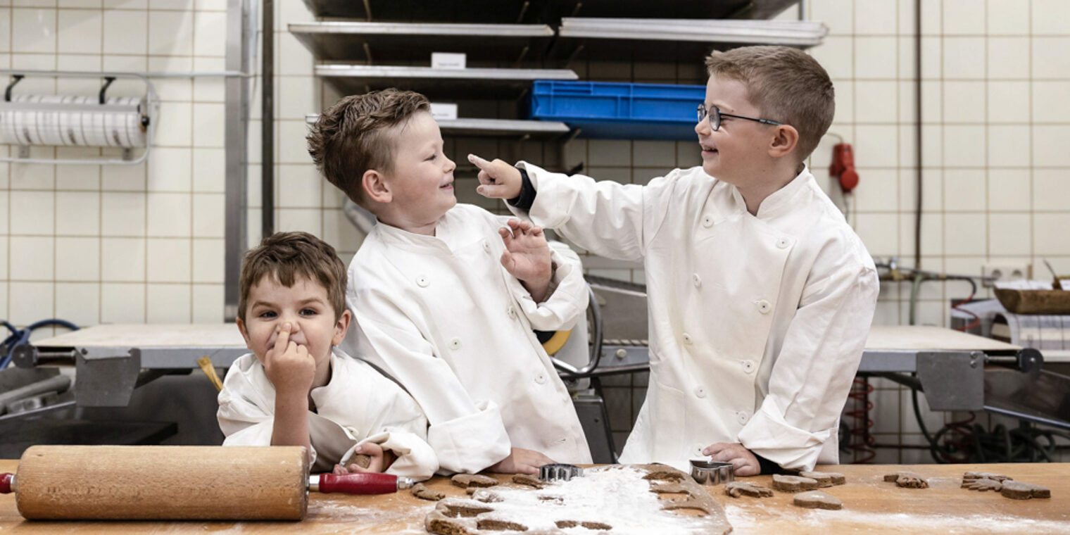 Der Kita-Wettbewerb des Handwerks verspricht allen Beteiligten viel Spaß. Drei Kinder stehen in einer Bäckerei hinter einem Tisch. Auf dem Tisch liegen ein Nudelholz und Teig.