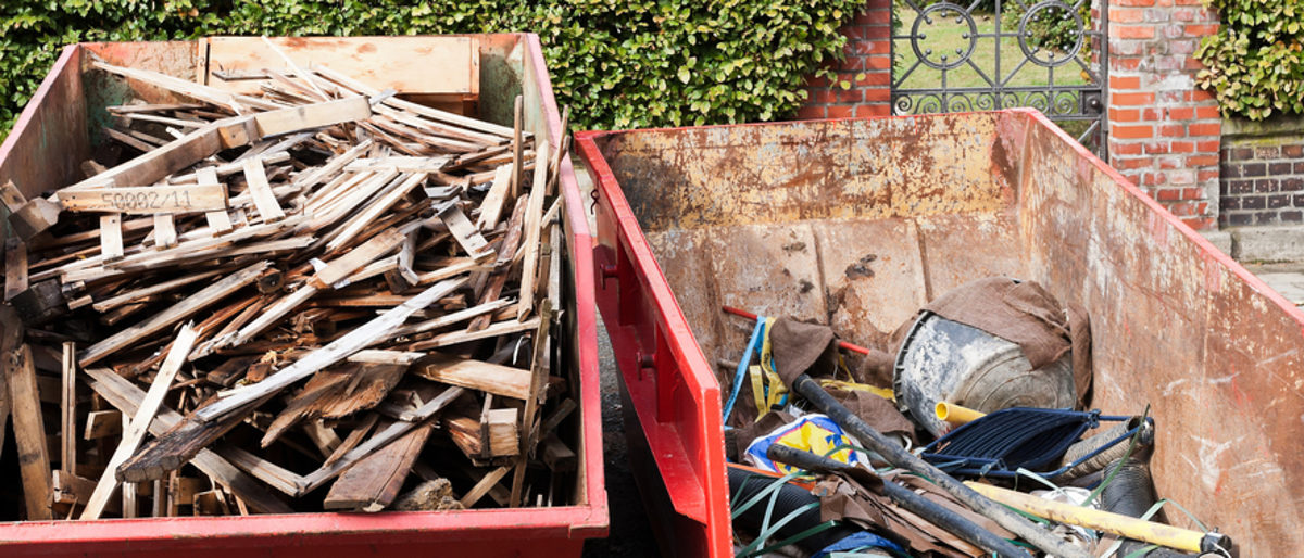 Handwerker müssen beim Transport von Abfällen einige Vorschriften beachten. zwei rote Müllcontainer, einer mit verschiedenen Holzteilen, der andere mit Metallschrott gefüllt.