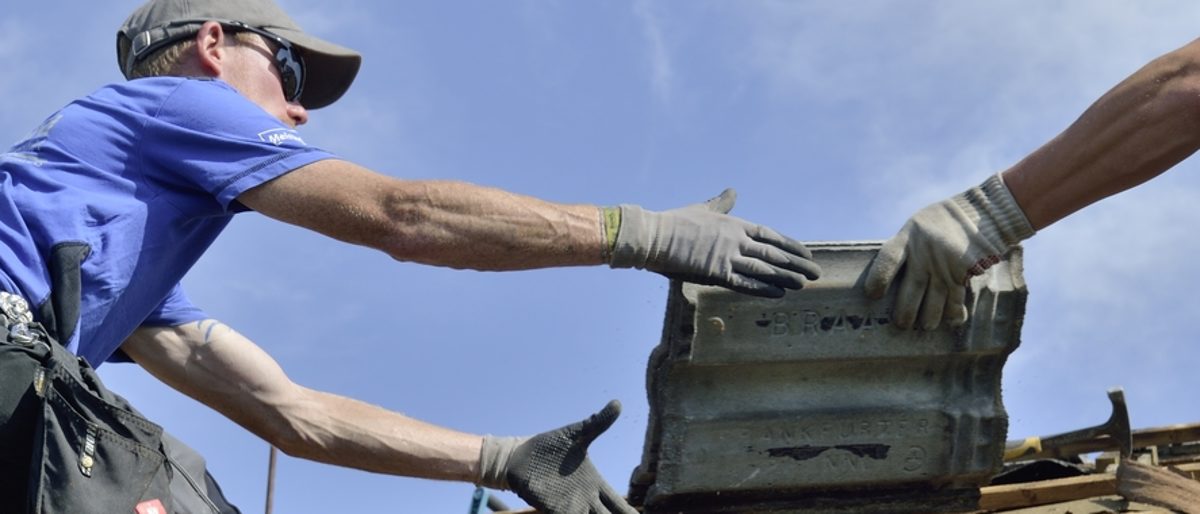Das Handwerk organisiert sich selbst. Ein Dachdecker greift nach Ziegeln.