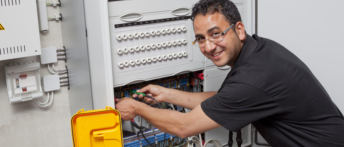 Elektroniker - ein Handwerksberuf mit viel Verantwortung und Freude. Elektroniker kniet vor einem Sicherheitskasten und verbindet Kabel.