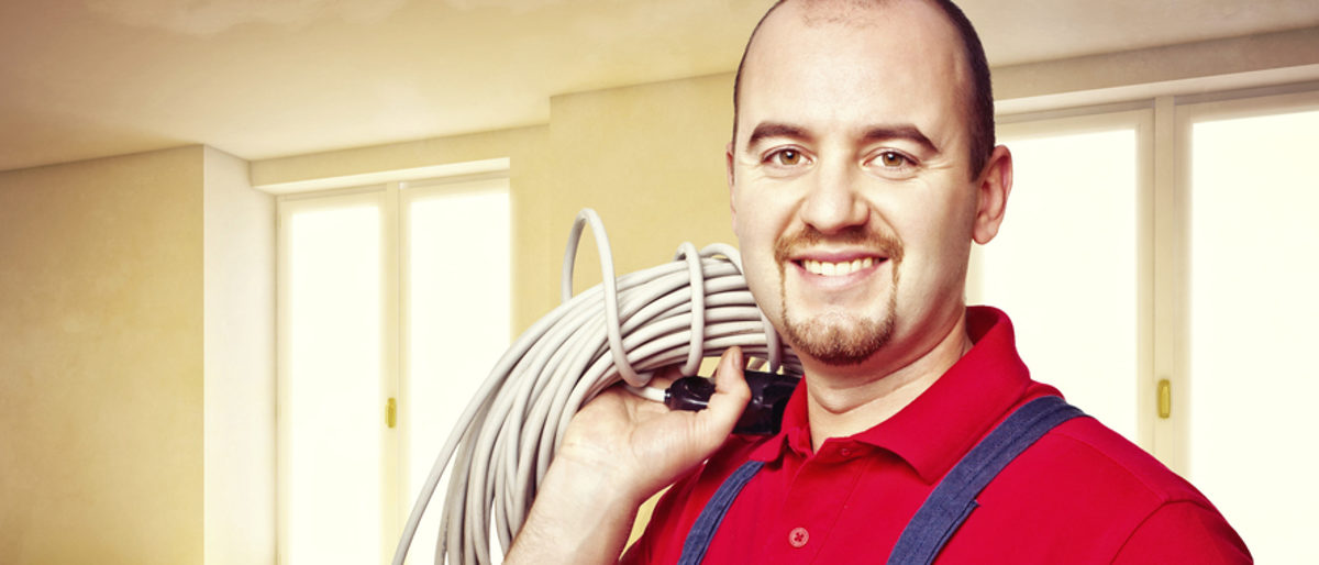 Das Versorgungswerk bietet Handwerkern günstige Vorsorgemöglichkeiten. Ein Mann in rotem Hemd steht in einem Raum. Er trägt ein aufgerolltes weißes Kabel über der Schulter, lächelt in die Kamera.