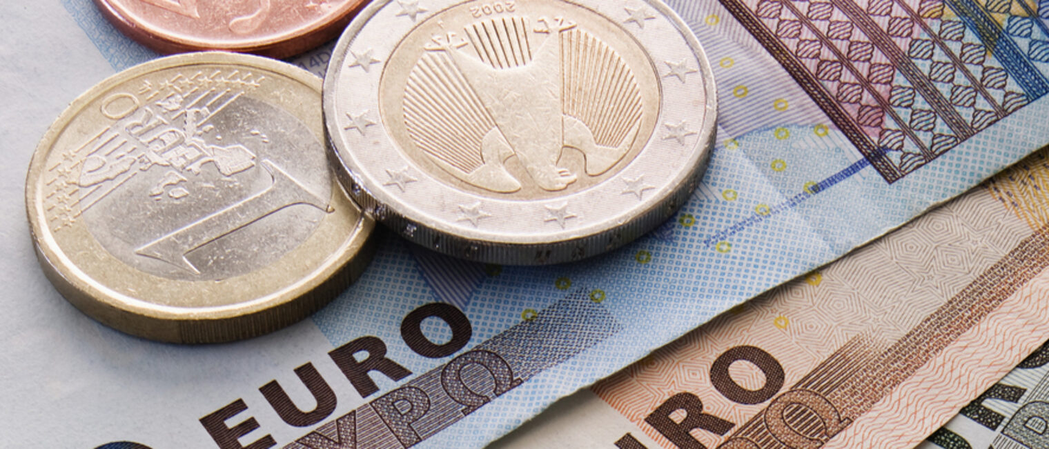 Zwei Geldmünzen liegen auf drei Geldscheinen. Die Währung ist Euro.