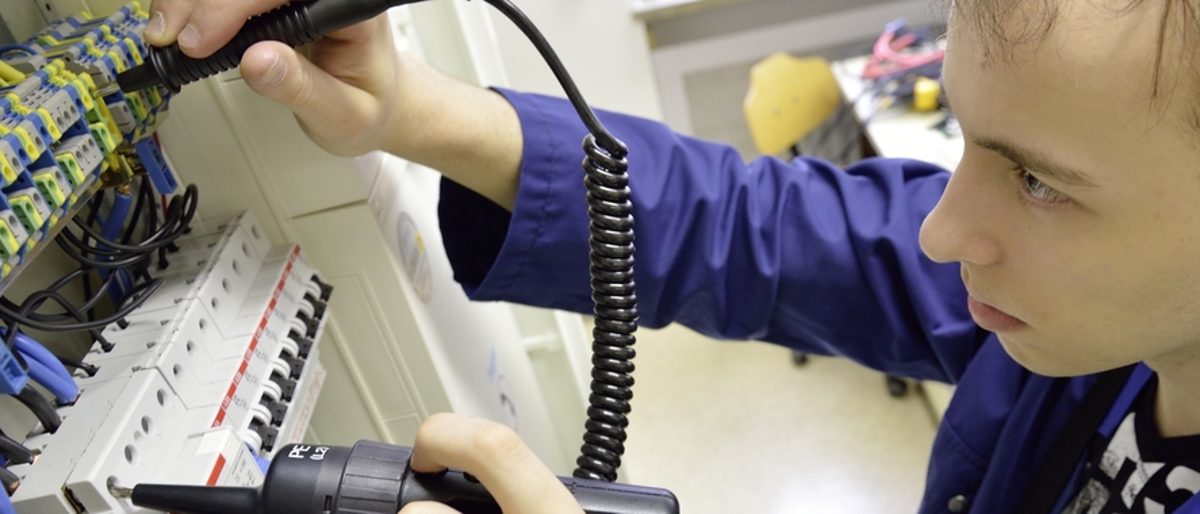 Beim Leistungswettbewerb zeigen junge Handwerker, was sie können. Ein junger Mann sieht konzentriert in einen Stromkasten. In beiden Händen hat er Werkzeuge zum Messen von Strom.