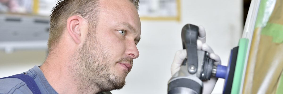 Fahrzeugbaumechaniker poliert etwas am Fahrzeug. Seitl. Nahaufna, Poliergerät erkennbar. Fahrzeug sieht man nicht