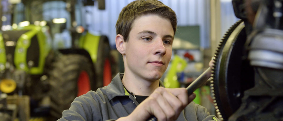 Die Zahlen zur Ausbildung im Handwerk der Region Heilbronn-Franken. Junger Mann zieht in einer Werkstatt mit Werkzeug eine Schraube an. Im Hintergrund sieht man unscharf einen Traktor.
