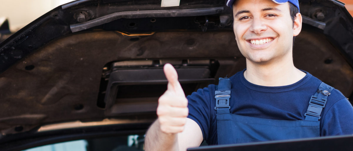 Existenzgründung im Nebenerwerb hat Vorteile Kfz-Mechaniker lehnt an geöffneter Motorhaube mit Laptop, strahlend zeigt er mit der Hand den Daumen hoch.