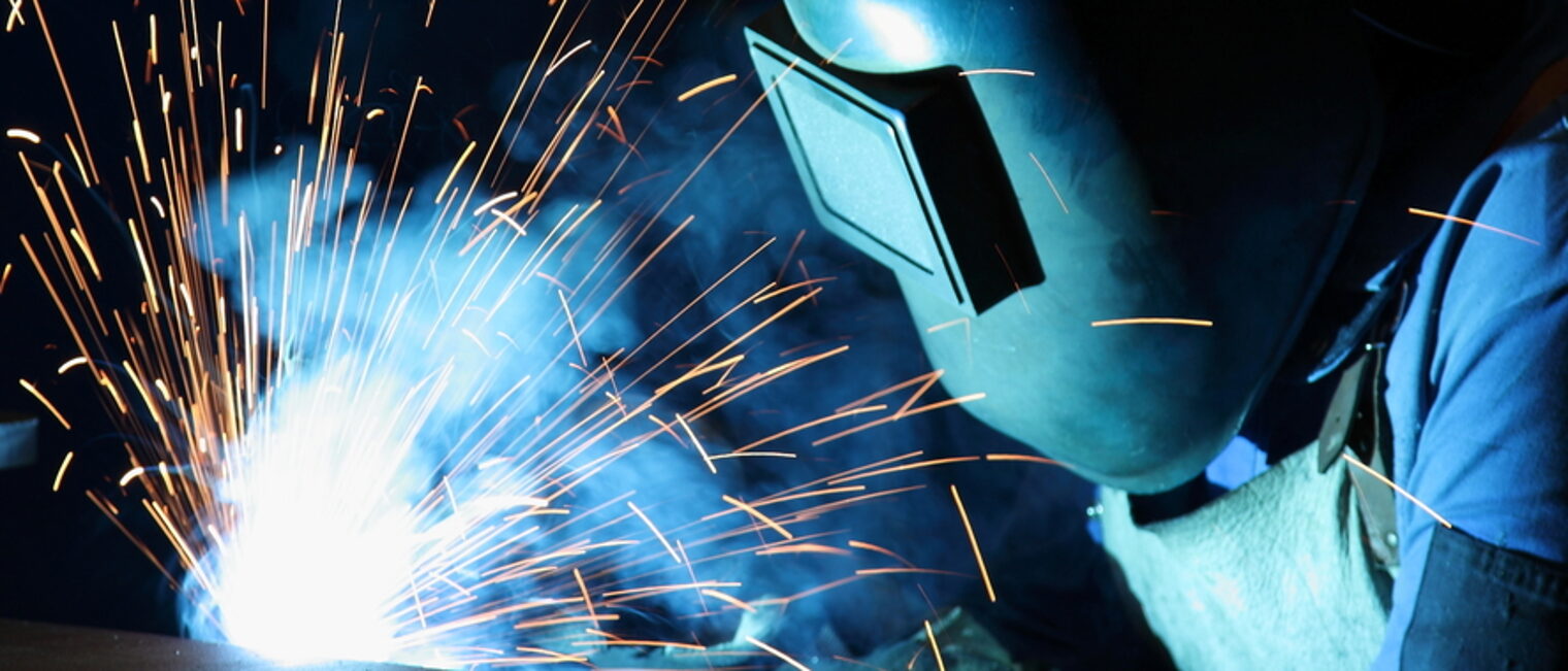 Zur Ausbildung von Metallbauern gehört das Schweißen. Metallbauer trägt Schutzbrille beim Schweißen mit Funkenflug