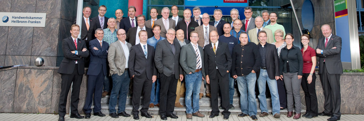 Die Vollversammlung der Handwerkskammer Heilbronn-Franken. Eine große Gruppe Menschen steht aufgereiht auf den Stufen zum Eingang eines Gebäudes. Alle lächeln in die Kamera.