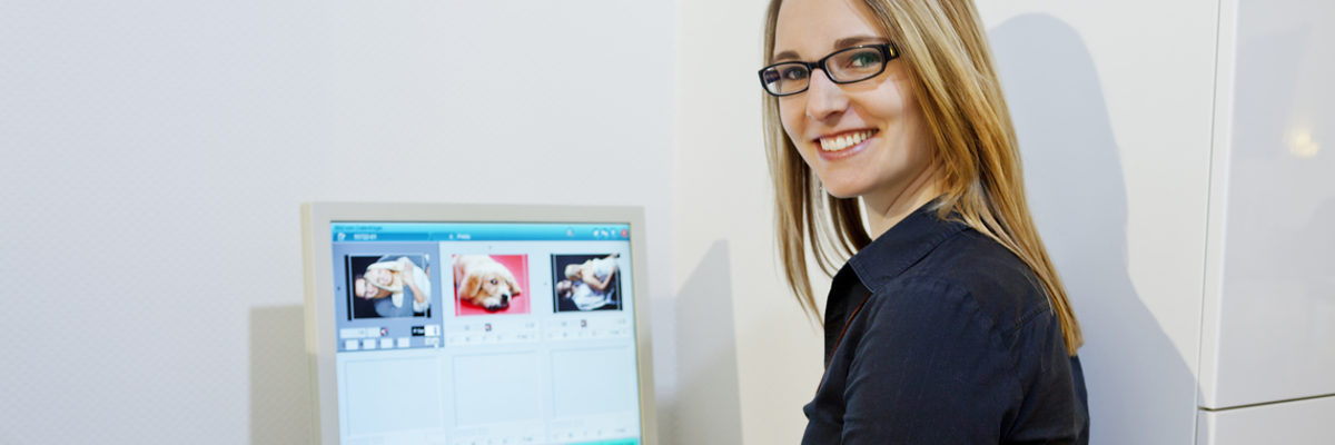 Pressefotos der Handwerkskammer Heilbronn-Franken für Redaktionen. Blonde Frau mit Brille sitzt vor einem Bildschirm, auf dem drei Fotos zu sehen sind. Sie hat sich halb zur Kamera umgedreht.