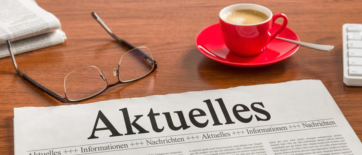 Hier bekommen Pressevertreter aktuelle Informationen aus dem Handwerk. Eine Zeitung, eine Lesebrille, eine rote Tasse mit Kaffee, eine Tastatur und ein Stift liegen auf einer Holzoberfläche.