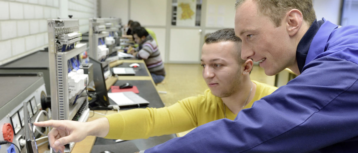 Freie Ausbildungs- oder Praktikumsplätze finden Bewerber hier. In einem Schulungsraum sind zwei Männer im Vordergrund im Profil zu sehen. Sie sehen sich etwas auf einem Bildschirm an.