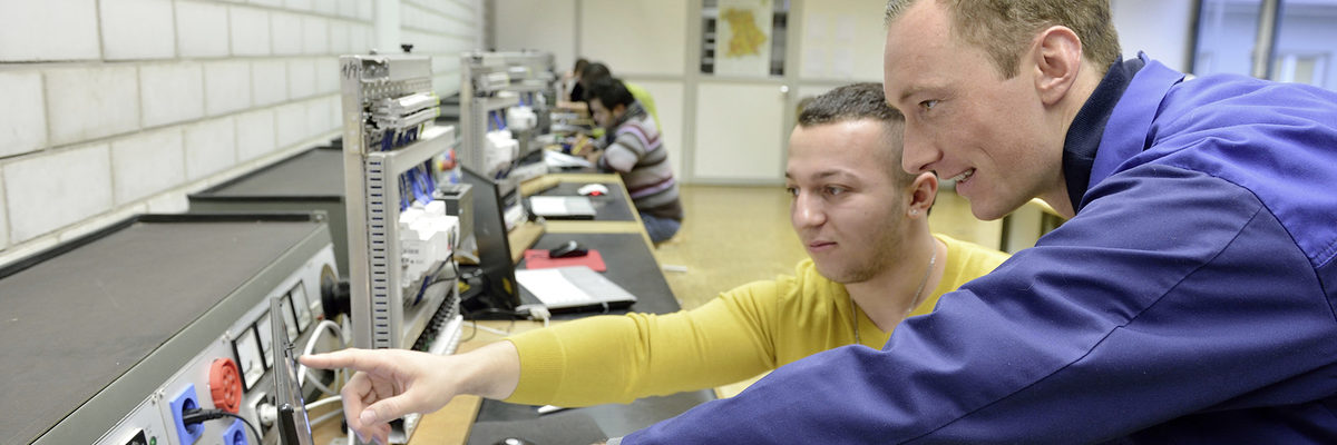 Freie Ausbildungs- oder Praktikumsplätze finden Bewerber hier. In einem Schulungsraum sind zwei Männer im Vordergrund im Profil zu sehen. Sie sehen sich etwas auf einem Bildschirm an.