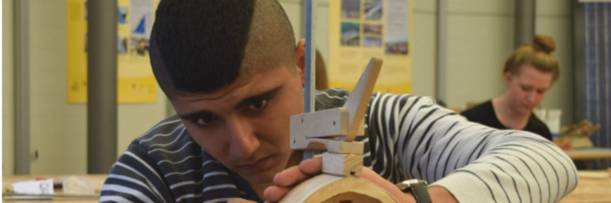 Werkstatt-Tage für Flüchtlinge Ein junger Mann schaut auf ein hält ein Werkstück aus Holzteilen in der Hand und schaut darauf.
