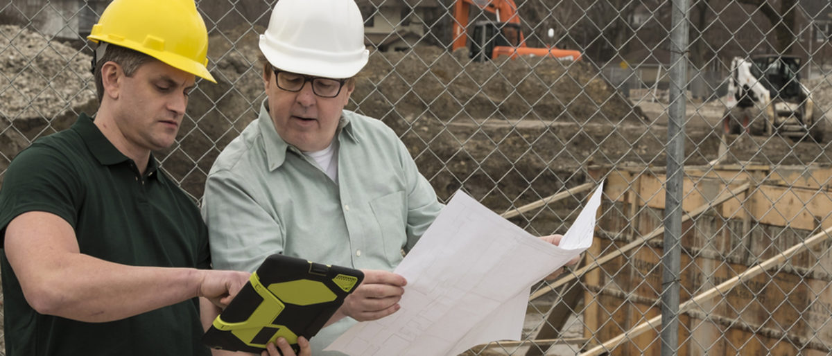 Zum 1. Januar 2018 ist die größte Reform des Bauvertragsrechts in Kraft getreten. Zwei Männer mit Helmen schauen auf einen Plan. Im Hintergrund ist eine Baustelle zu sehen.