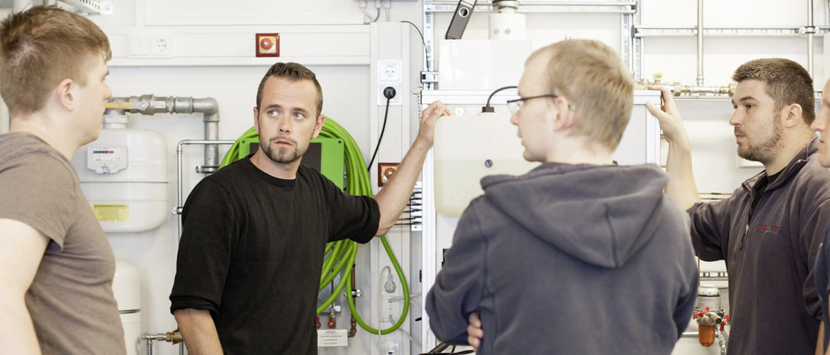 Die Handwerksjunioren wollen das Handwerk mitgestalten und dafür werben Fünf junge Männer stehen in einem Raum mit Geräten. Vier davon schauen den Mann ganz links an, der scheinbar etwas sagt.