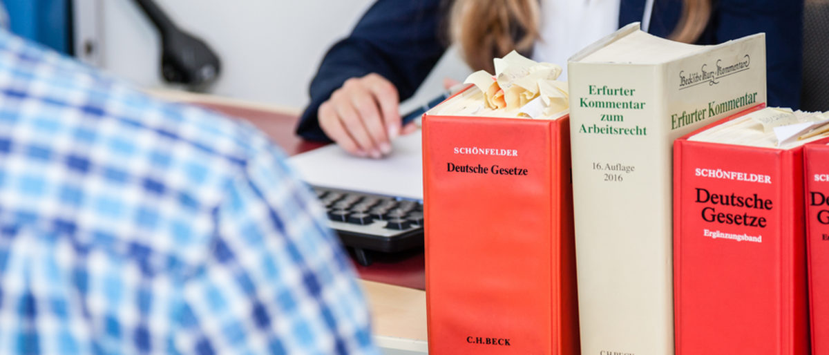 Gesetz stärkt Rechte der Handwerker Vier dicke Gesetzesbücher stehen rechts vorn im Bild. Im Hintergrund sieht man eine Frauenhand, die einen Stift hält.