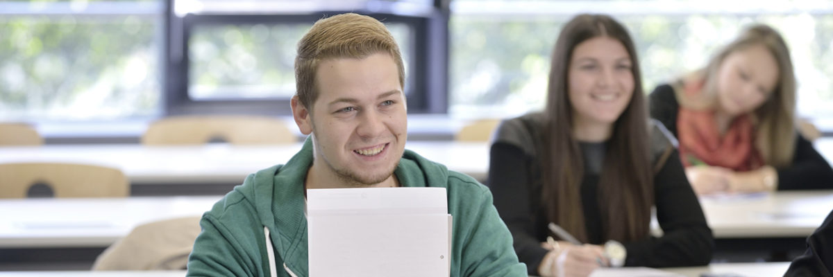 Schüler, grüner Pulli, Block, Händen, Hintergrund, zwei Schülerinnen, mit Einverständniserklärung, Schulung, Kurs, ÜBA, Lehrgang