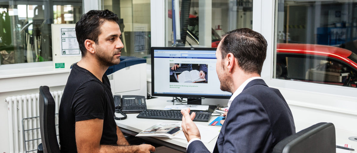 Betriebe erhalten in der Personalberatung individuelle Hilfestellung. Zwei Männer sitzen in einem Werkstatt-Büro am Tisch und sprechen miteinander.