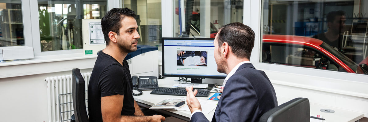 Betriebe erhalten in der Personalberatung individuelle Hilfestellung. Zwei Männer sitzen in einem Werkstatt-Büro am Tisch und sprechen miteinander.