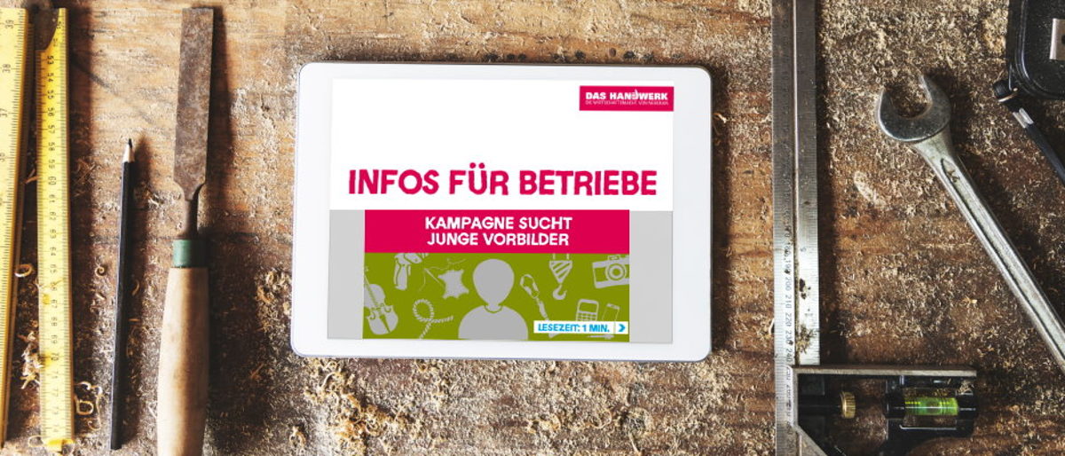 Alle zwei Monate gibt es die "Infos für Betriebe" der Imagekampagne. Tablet-PC liegt auf einer Werkbank aus Holz umgeben von Werkzeugen. Der Bildschirm zeigt das Logo "Infos für Betriebe".