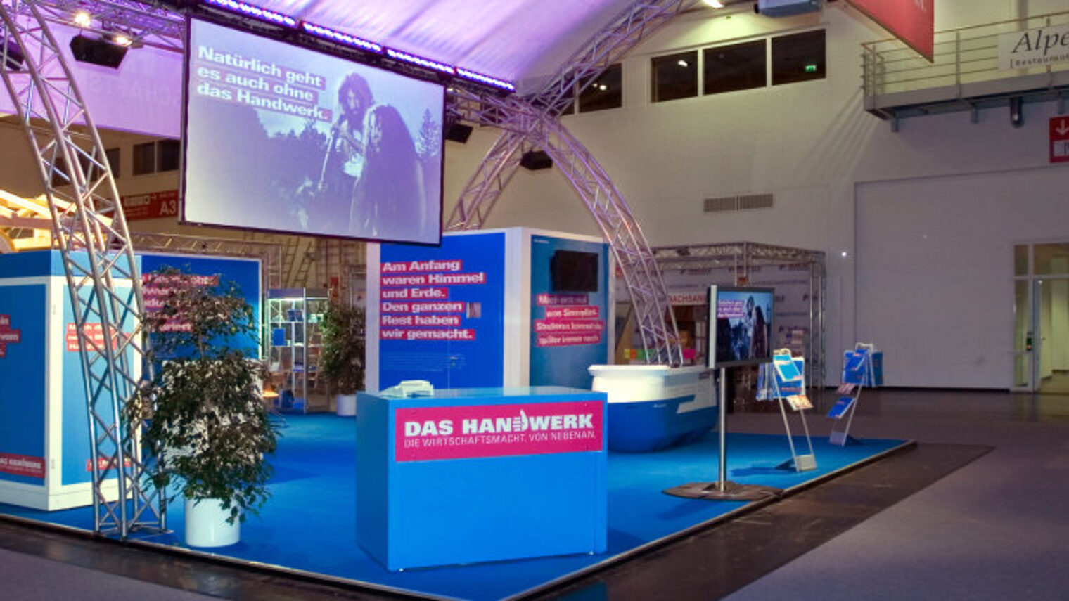Großer Messestand mit verschiedenen Elementen in den Farben blau und rot der Imagekampagne in einer noch leeren Messehalle.