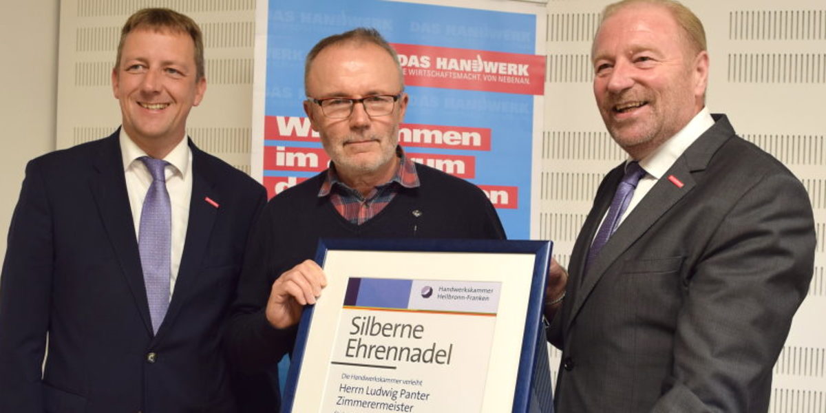 Ludwig Panter (M.) erhielt die Silberne Ehrennadel der Handwerkskammer Drei Männer stehen zusammen vor einem Roll-Up und präsentieren eine Urkunde mit der Aufschrift "Silberne Ehrennadel".