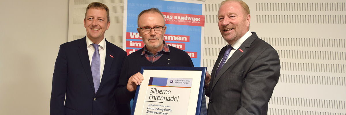 Ludwig Panter (M.) erhielt die Silberne Ehrennadel der Handwerkskammer Drei Männer stehen zusammen vor einem Roll-Up und präsentieren eine Urkunde mit der Aufschrift "Silberne Ehrennadel".