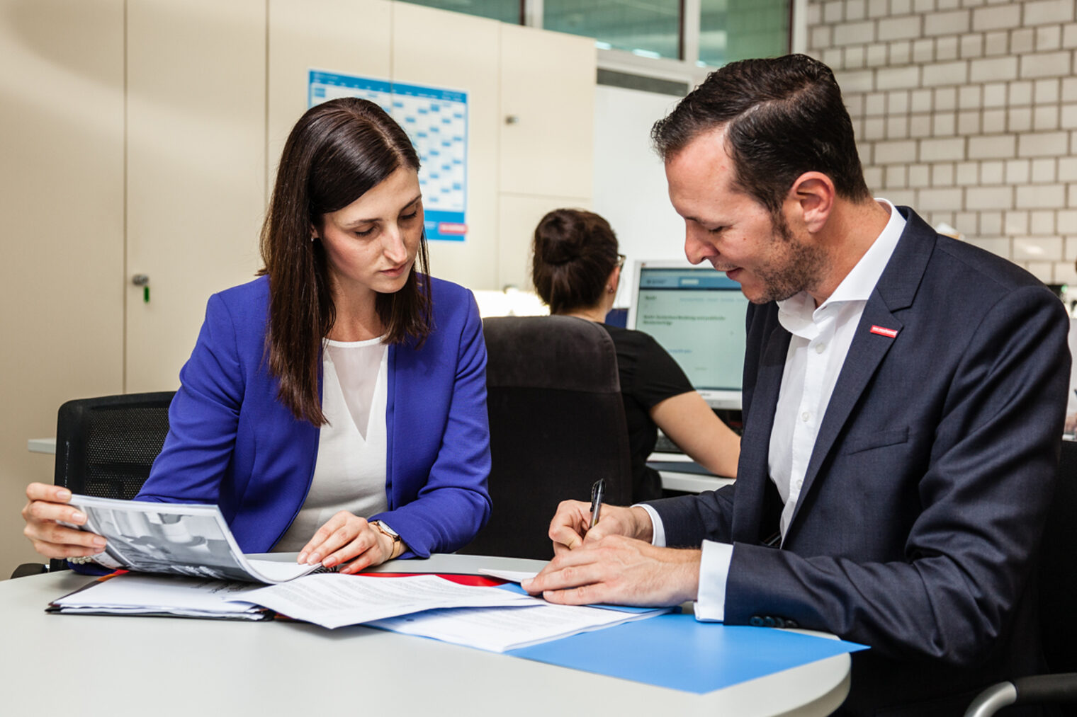 Beratungssituation: ein Mann und eine Frau sitzen gemeinsam am Tisch. Der Mann schreibt etwas auf.