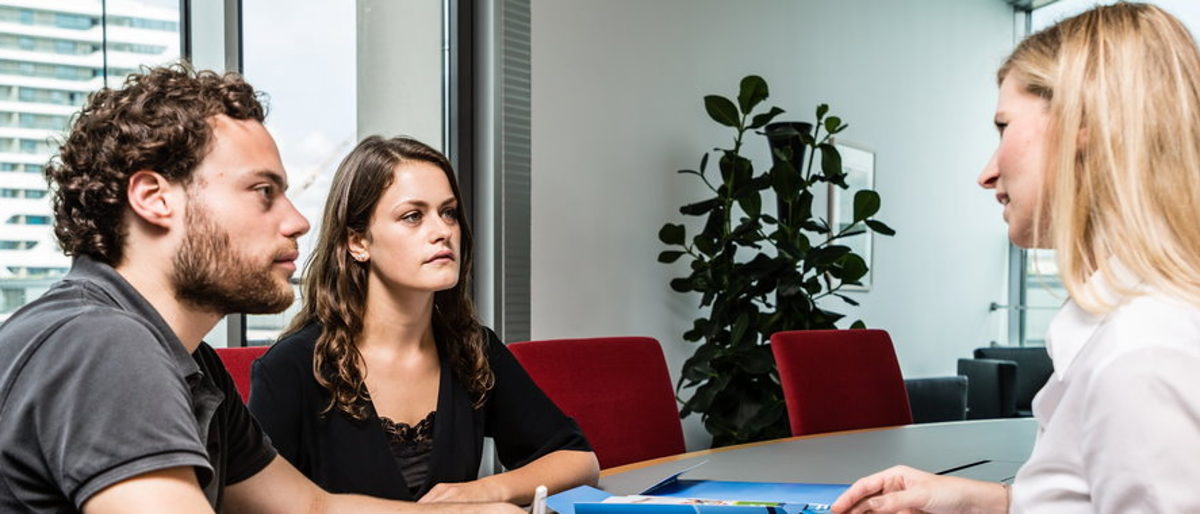 Die Betriebsberater beraten zu betriebswirtschaftlichen und technischen Fragen. Eine Frau und zwei Personen sitzen an einem Besprechungstisch, auf dem Tisch liegen Unterlagen