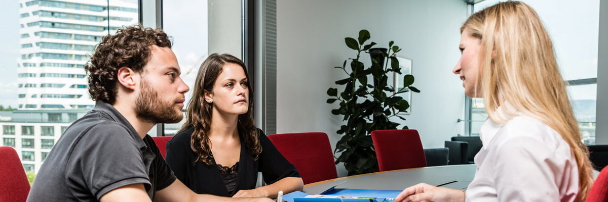 Die Betriebsberater beraten zu betriebswirtschaftlichen und technischen Fragen. Eine Frau und zwei Personen sitzen an einem Besprechungstisch, auf dem Tisch liegen Unterlagen