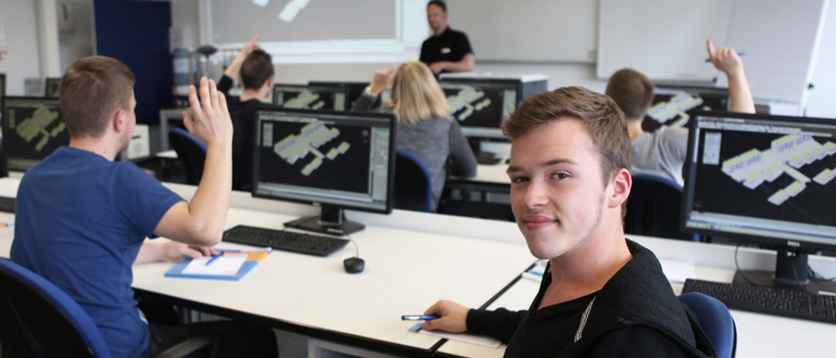 Azubis können in der Ausbildung zusätzliche Qualifikationen erwerben. Moderner Unterrichtsraum mit Schülern ist von hinten zu sehen. Ein Schüler hat sich umgedreht und blickt in die Kamera.