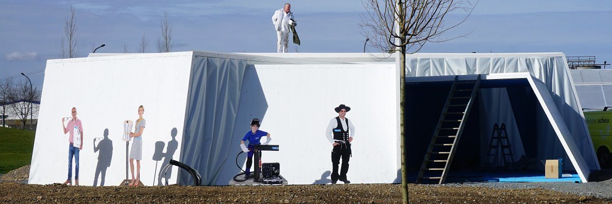 Der Pavillon des Handwerks auf der Bundesgartenschau 2019 in Heilbronn Eine weißgestrichene Holzkonstruktion ist von außen zu sehen. Auf dem Dach steht ein Mann in weißer Arbeitskleidung.