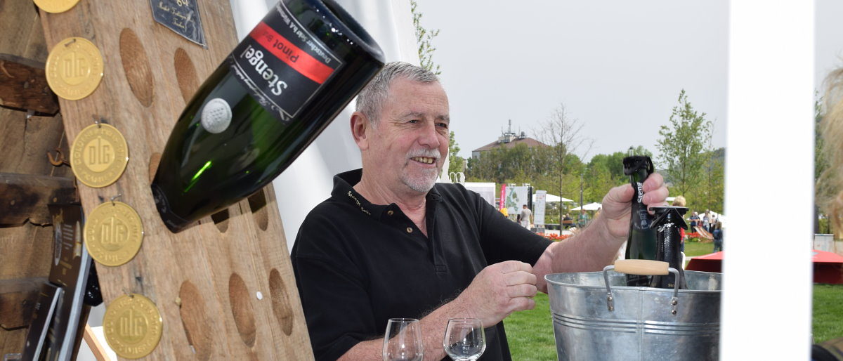 Sektverkostung im Pavillion des Handwerks der Kellerei Stengel Stengel-Sektflasche steckt in Rüttelpult, am Ausschank Mann mit Sektflasche in der Hand.