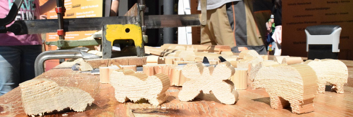 Bei der Schreinerinnung Hohenlohe konnten die Schüler Figuren sägen. Auf einem Biertisch sind im Vordergrund verschiedene Figuren aus Holz zu sehen. Im Hintergrund steht eine Handsäge.