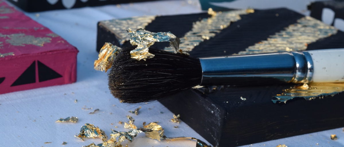 Mitmachen und einfach mal ausprobieren kam bei den Besuchern gut an. Ein Pinsel mit Goldflittern liegt auf einem Bild, geeigt wird wie man vergoldet.