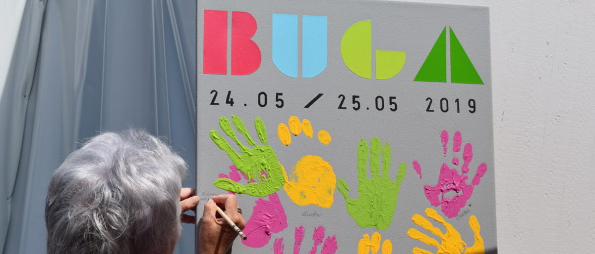 Der Handabdruck von B. Huber aus der Schweiz ist Teil des Kunstwerks. Eine Besucherin schreibt unter ihren Handabdruck Name und Wohnort, es entsteht ein Kunstbild