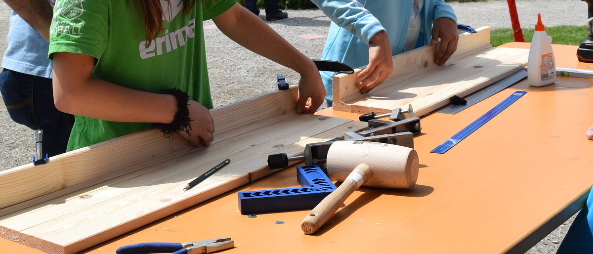 Sichtlich Spaß hatten kleine und große Leute beim Regal-Bau. Kinderhände, die Schraubzwingen an Holzbrettern befestigen.