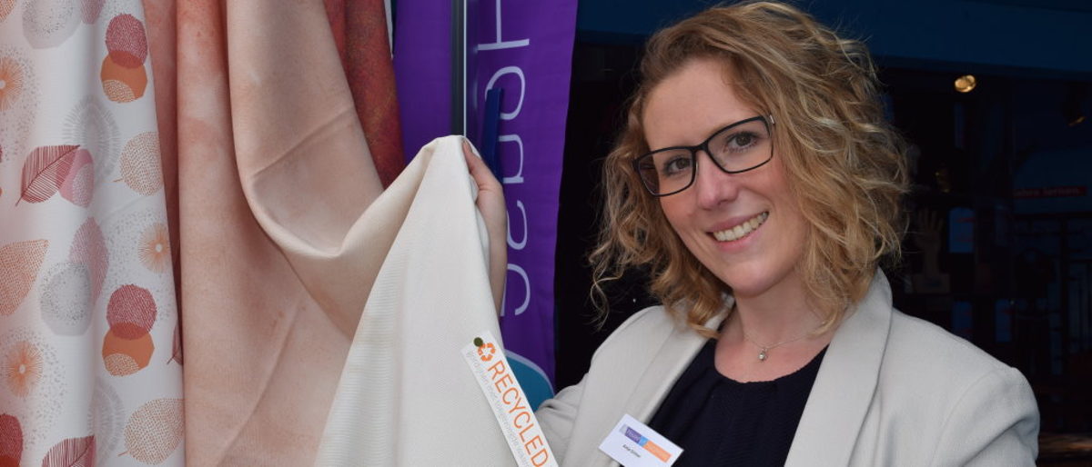 Antje Gröner präsentiert trendige Recycling Vorhang-Kollektion Frau schaut lächelnd in die Kamera und hält einen Recycling-Stoff hoch