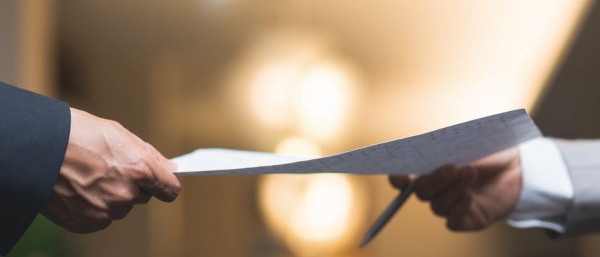 Verhaltenskodex für das Ehren- und Hauptamt der Handwerkskammer. Eine Hand hält ein Blatt Papier. Eine zweite Hand hält einen Kugelschreiber und greift danach.