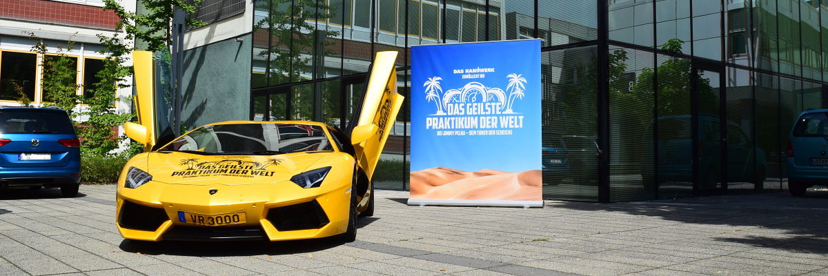 Das Handwerk ermöglicht diesen Sommer das geilste Praktikum der Welt. Ein gelber Lamborghini steht mit offenen Flügeltüren vor einem Gebäude. Im Hintergrund ein Plakat mit einem Wüstenmotiv.