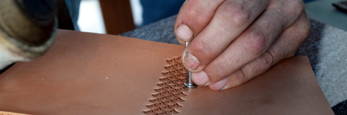 Mit dem Punziereisen entsteht ein schönes Shell-Muster. Ein Sattler punziert ein Stück Leder mit einem Punzier-Eisen im Shell-Muster.