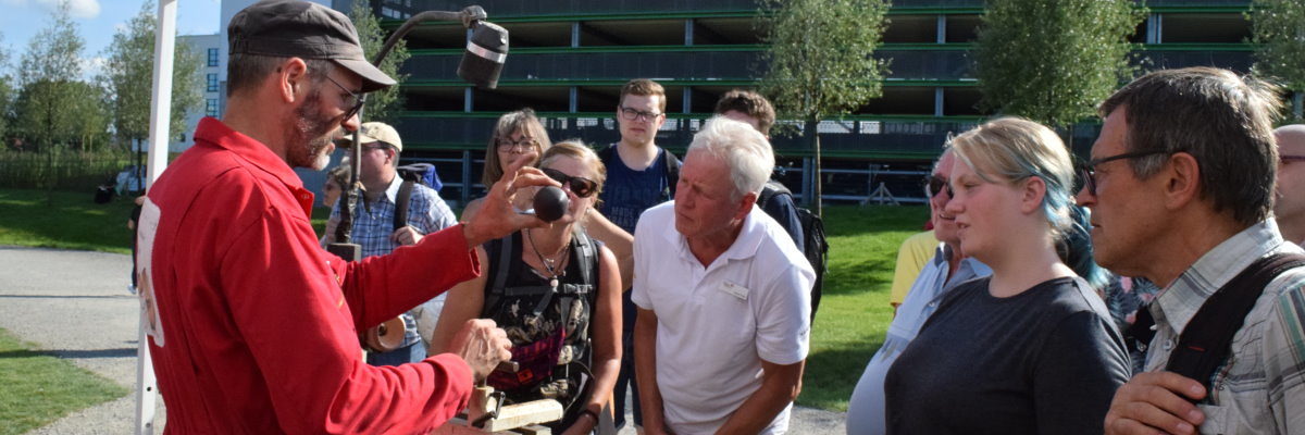 BUGA-Besucher schauen bei Entstehung von Holzkugeln an der Drehbank zu Ein Mann hält eine Kugel aus dunklem Holz in der Hand und zeigt sie einigen Menschen, die um ihn herum stehen.