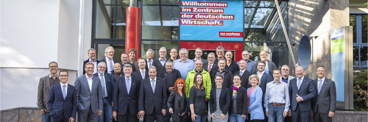 Die Vollversammlung der Handwerkskammer Heilbronn-Franken 2019-2024. Eine große Gruppe Menschen steht vor dem Eingang eines Gebäudes und lächelt in die Kamera.